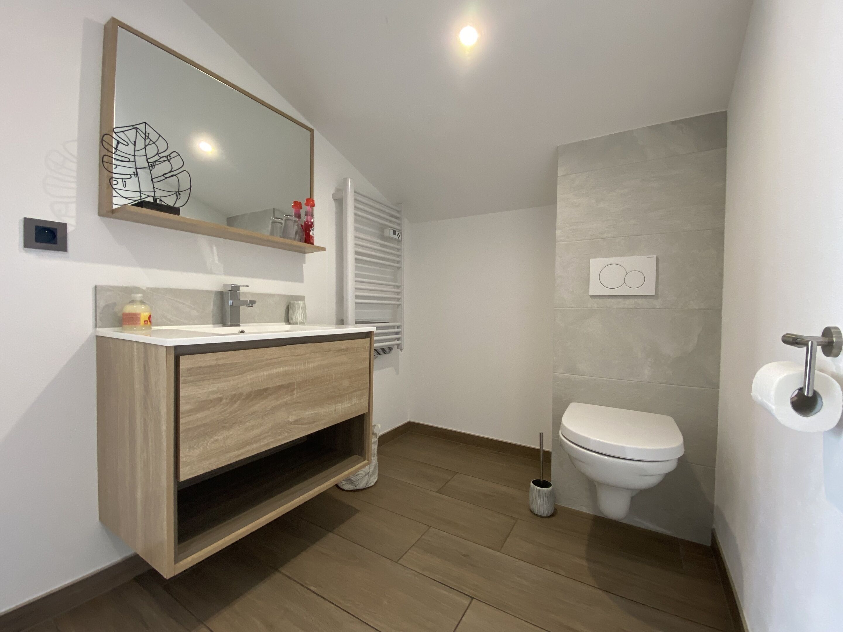 A modern bathroom with a wooden vanity, a toilet, and a mirror.