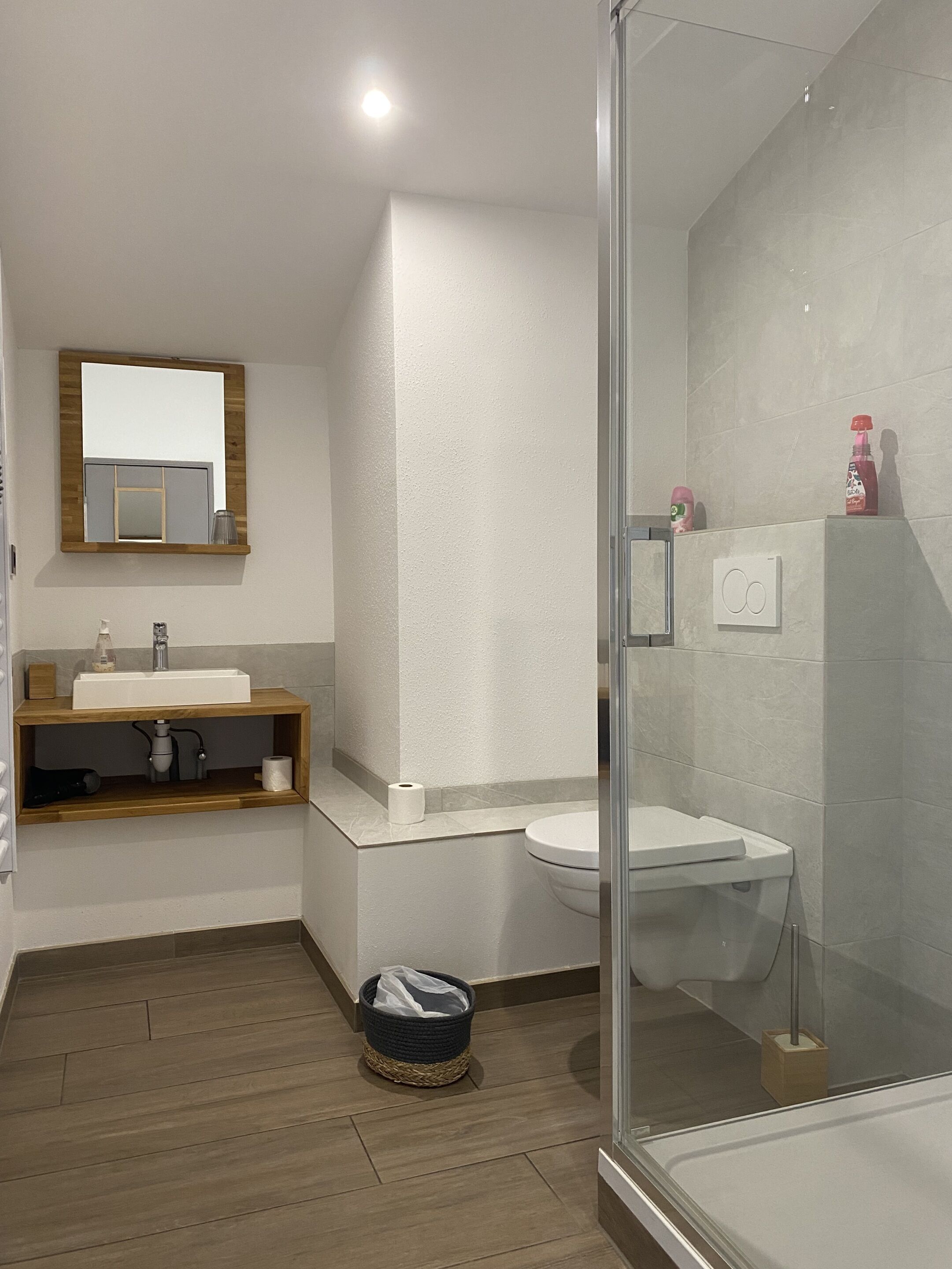 Une salle de bain moderne avec un meuble-lavabo en bois, un lavabo blanc, une cabine de douche en verre et un miroir au-dessus du meuble-lavabo.