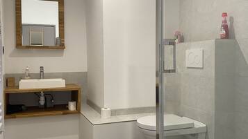 Une salle de bain moderne avec un meuble-lavabo en bois, un lavabo blanc, une cabine de douche en verre et un miroir au-dessus du meuble-lavabo.