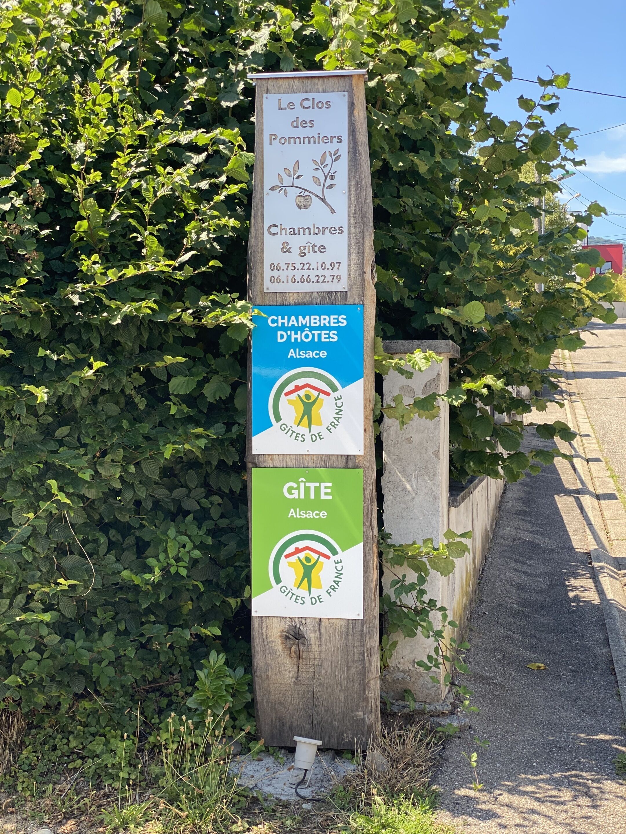 A wooden signpost with information about accommodations and a gîte in Alsace, France.