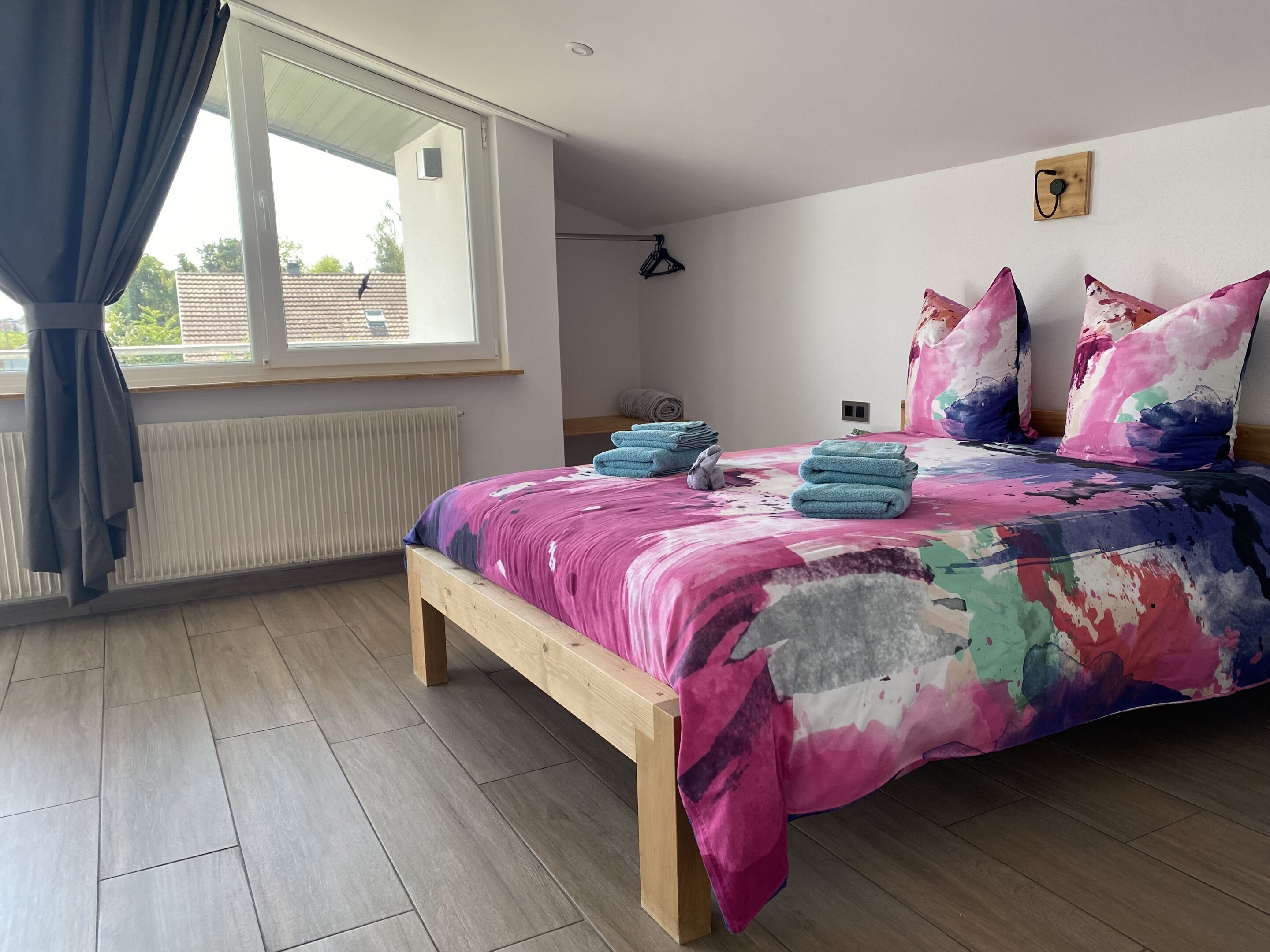A bedroom with a bed, a window with curtains, a radiator, and a wooden bench.