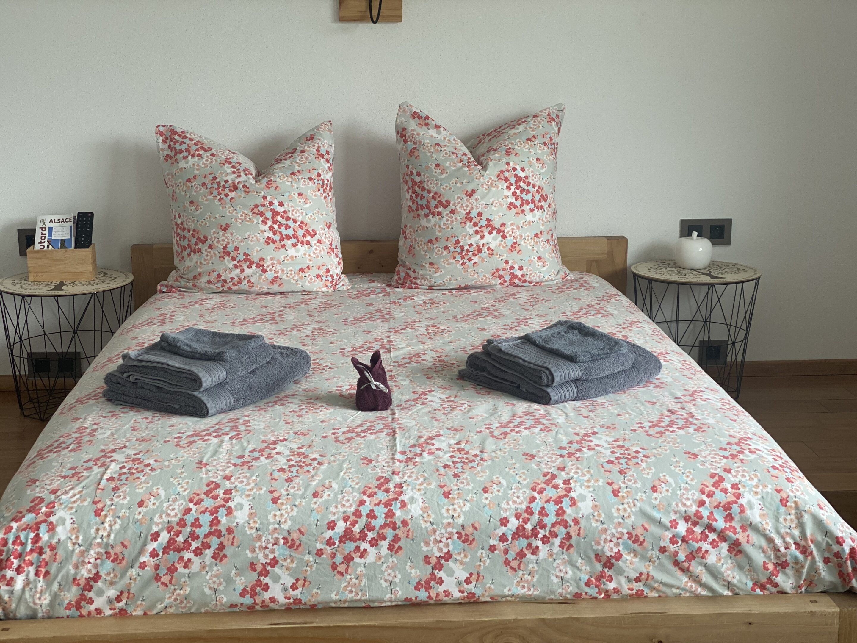 Een net opgemaakt bed met bloemenbeddels, twee kussens en opgevouwen handdoeken.