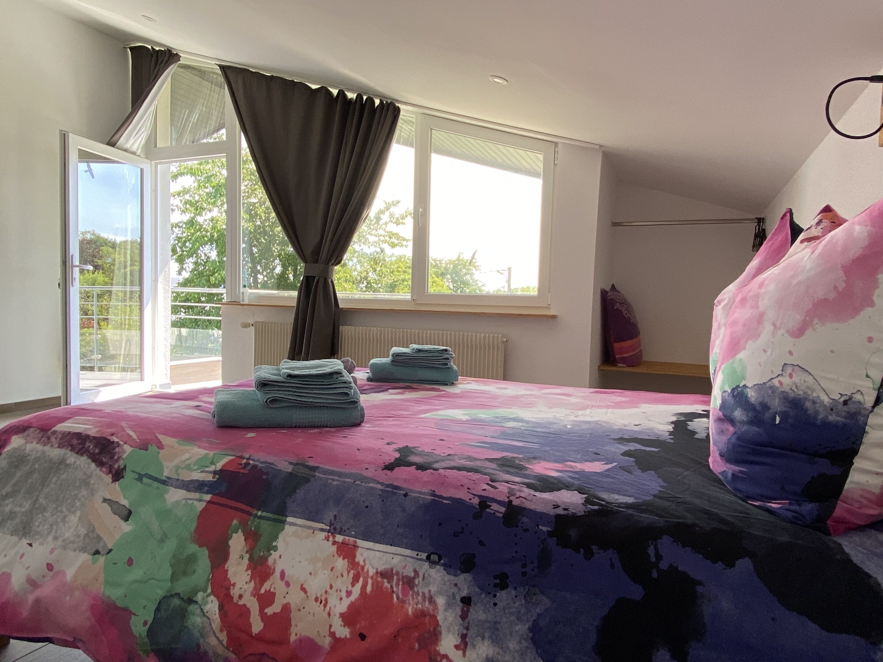 Una camera da letto con un letto, una finestra con tende, un termosifone e vista sul verde.