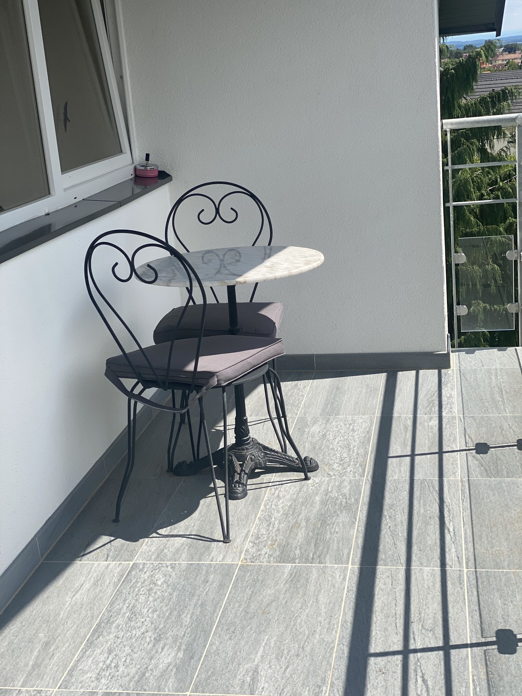 Un balcón con una mesa y dos sillas, una ventana y vistas a una zona residencial.