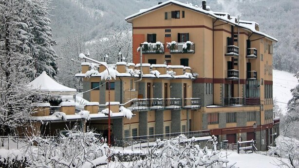Un edificio de varios pisos con balcones, rodeado de árboles cubiertos de nieve y montañas al fondo.