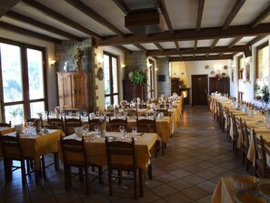A restaurant with multiple tables set for dining, wooden chairs, and a stone wall with a plant. - Hotel Cimone (Riolunato)