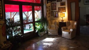 Una habitación acogedora con un toldo rojo, dos sillones, una mesa con lámpara y varias fotos enmarcadas en la pared.