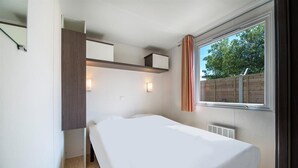A bedroom with a bed, built-in shelving, bedside lamps, and a window with curtains. - Camping le Chenal (Saint-Jean-de-Monts)