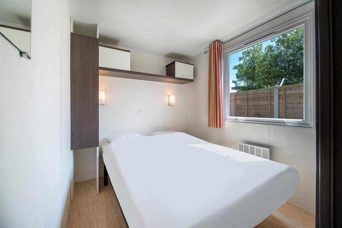 Un dormitorio con cama, estanterías empotradas, lámparas de noche y una ventana con cortinas.