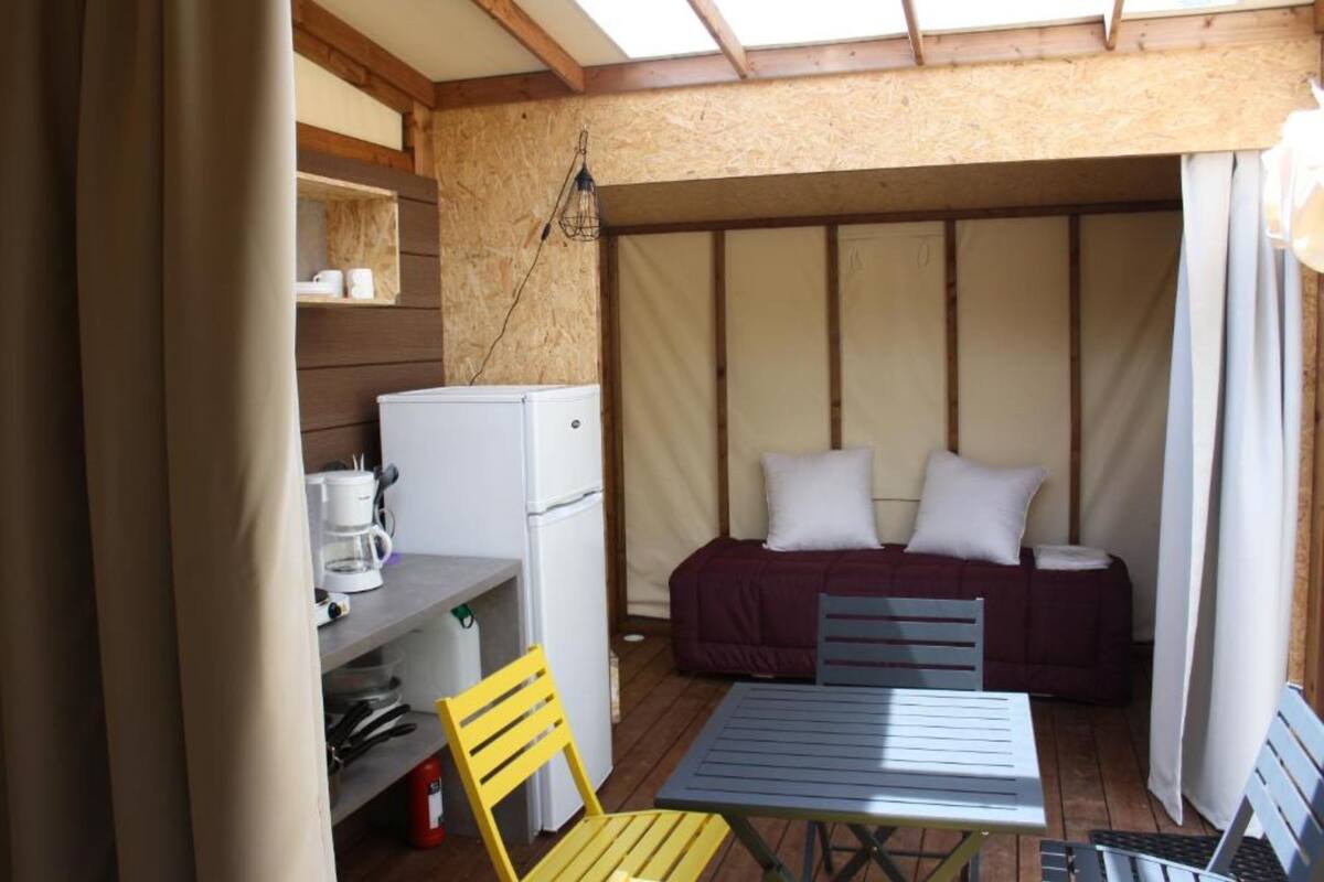 Una habitación pequeña y acogedora con cama, una mesa, una silla, un refrigerador y un estante con artículos de aseo.