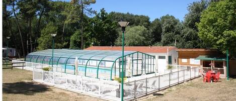 A greenhouse structure with a transparent roof, surrounded by a white fence, and adjacent to a small building with a red roof.