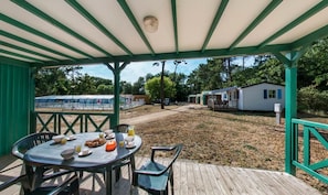 A covered outdoor area with a table set for breakfast, a wooden deck, and a view of mobile homes in the background.