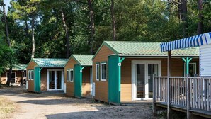 A row of cabins with green roofs and white trim, numbered 3 and 4, in a wooded area. - Camping le Chenal (Saint-Jean-de-Monts)
