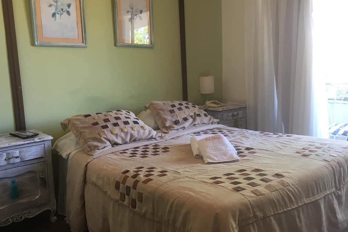 A neatly made bed with patterned pillows and a towel, a bedside table with a lamp, and two framed pictures on the wall.