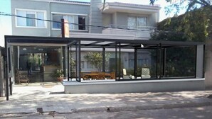 A modern house with a glass conservatory, a patio with furniture, and a view of a neighboring building.