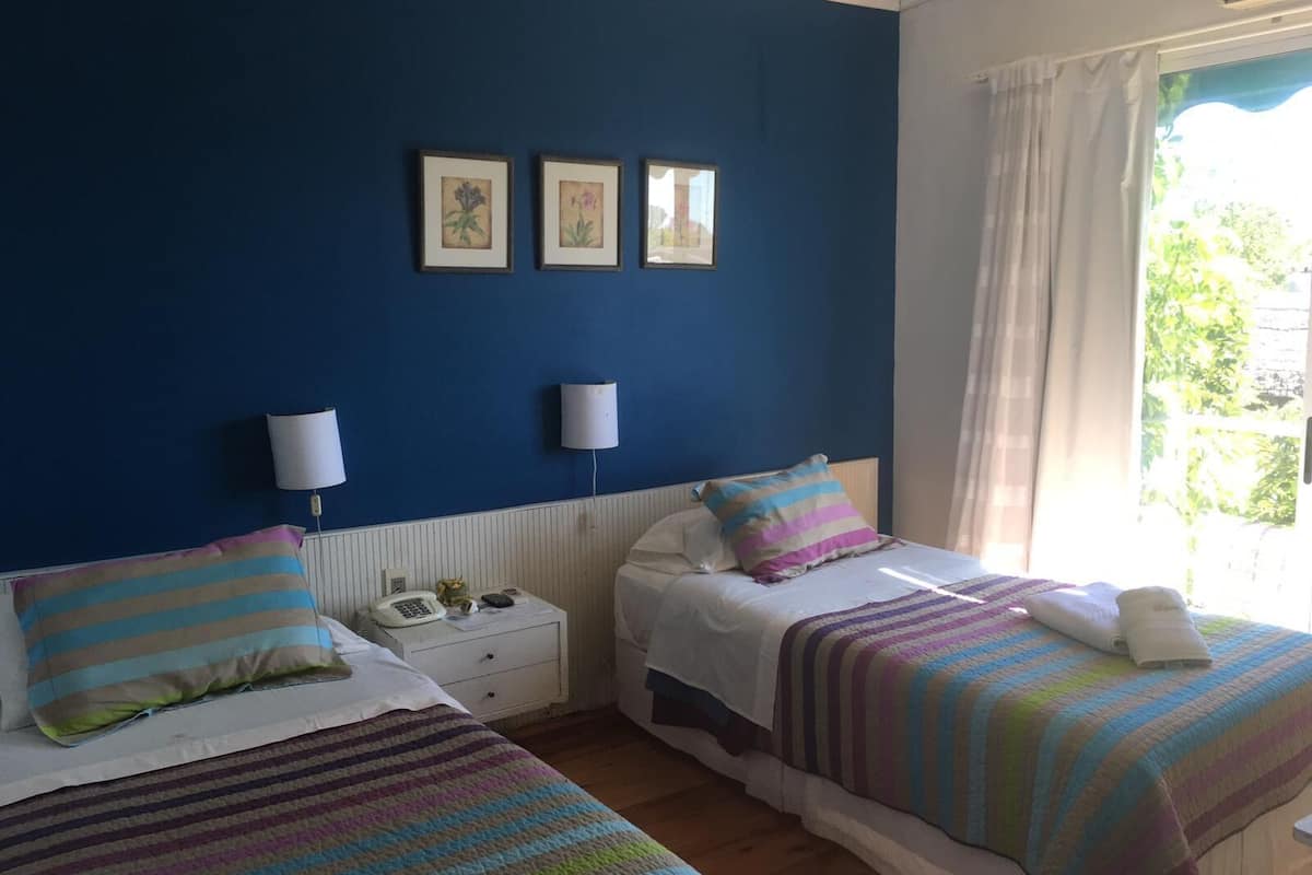 A room with two beds, a nightstand, and a window with curtains.