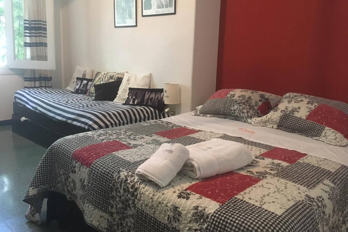 A bedroom with two beds, one with a striped bedspread and the other with a floral quilt. There are two framed pictures on the wall above the beds.