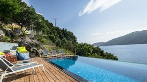 Ett trädäck med solstolar och en pool, med utsikt över en sjö och berg i bakgrunden.