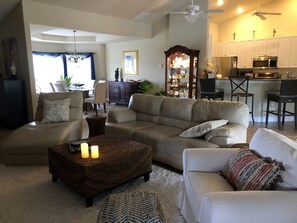 Relax in this stylish living room with a beige sofa, armchair, and coffee table, complemented by a dark cabinet and dining area.