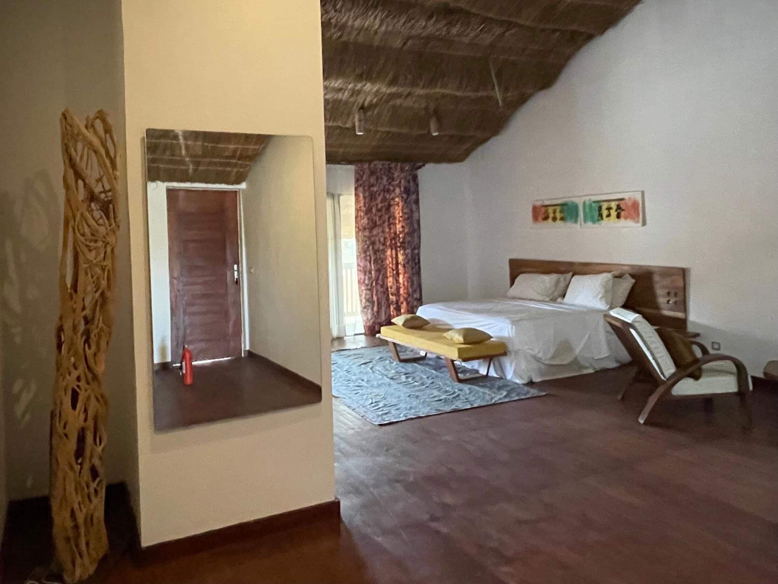 A bedroom with a bed, a bench, a chair, and a decorative wall hanging.
