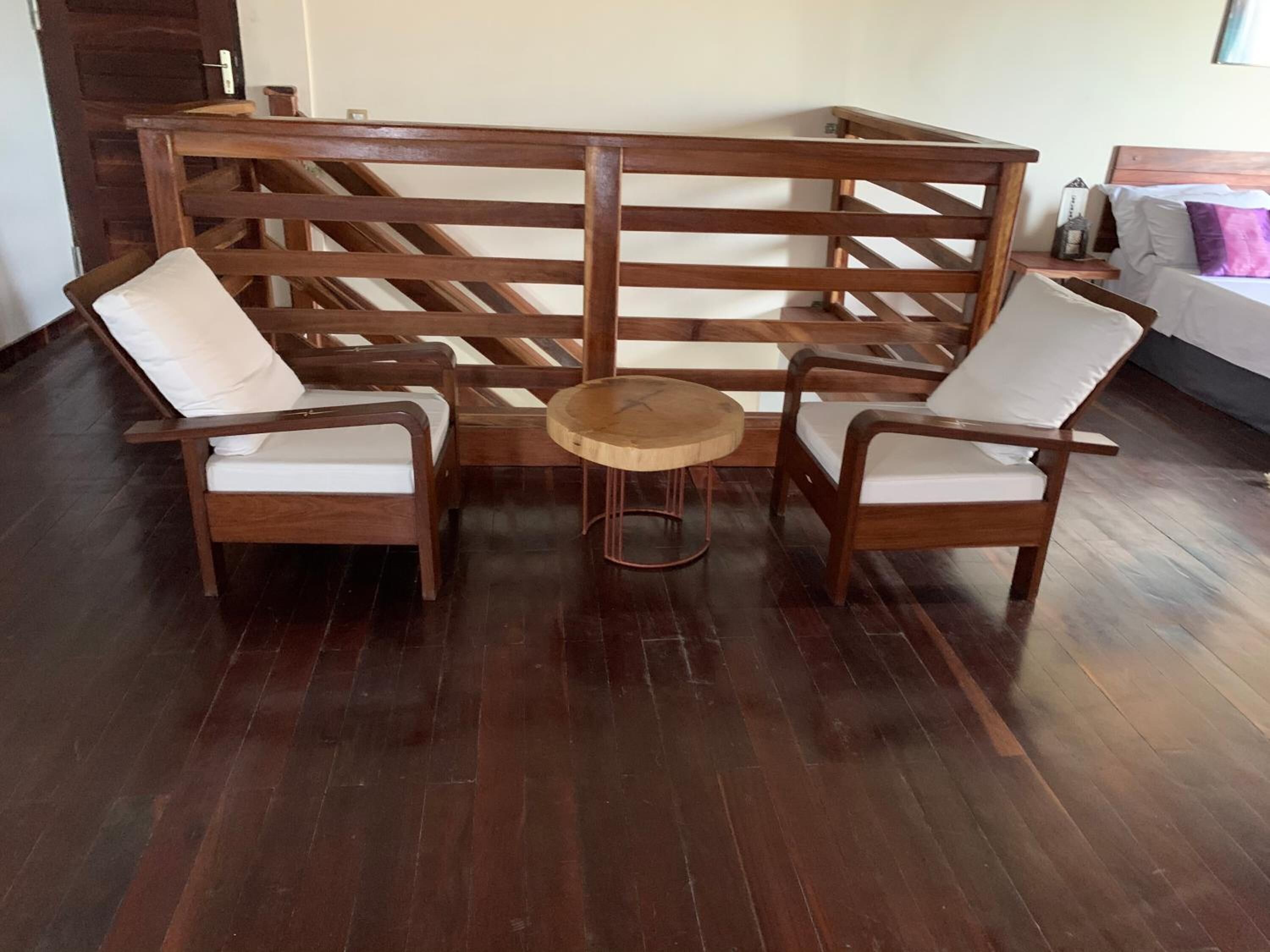 Une pièce avec un paravent en bois, deux fauteuils blancs rembourrés, une petite table ronde en bois et un lit avec un oreiller blanc et violet.
