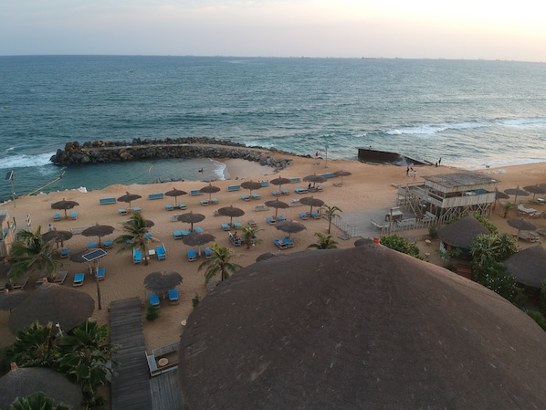 A beach with thatched umbrellas, sun loungers, and a wooden structure.