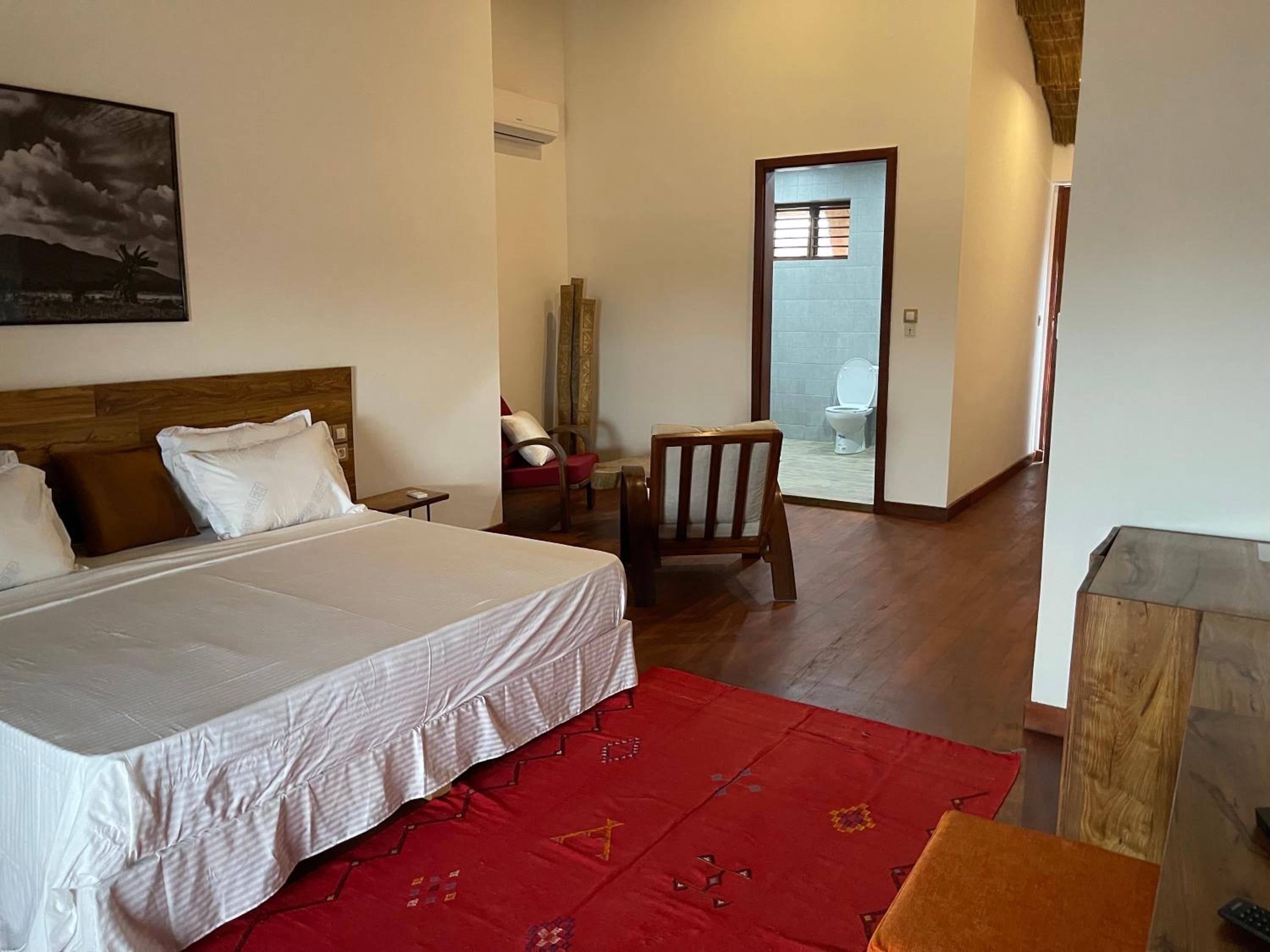 A hotel room with a large bed, a red patterned rug, a wooden chair, and a small table.