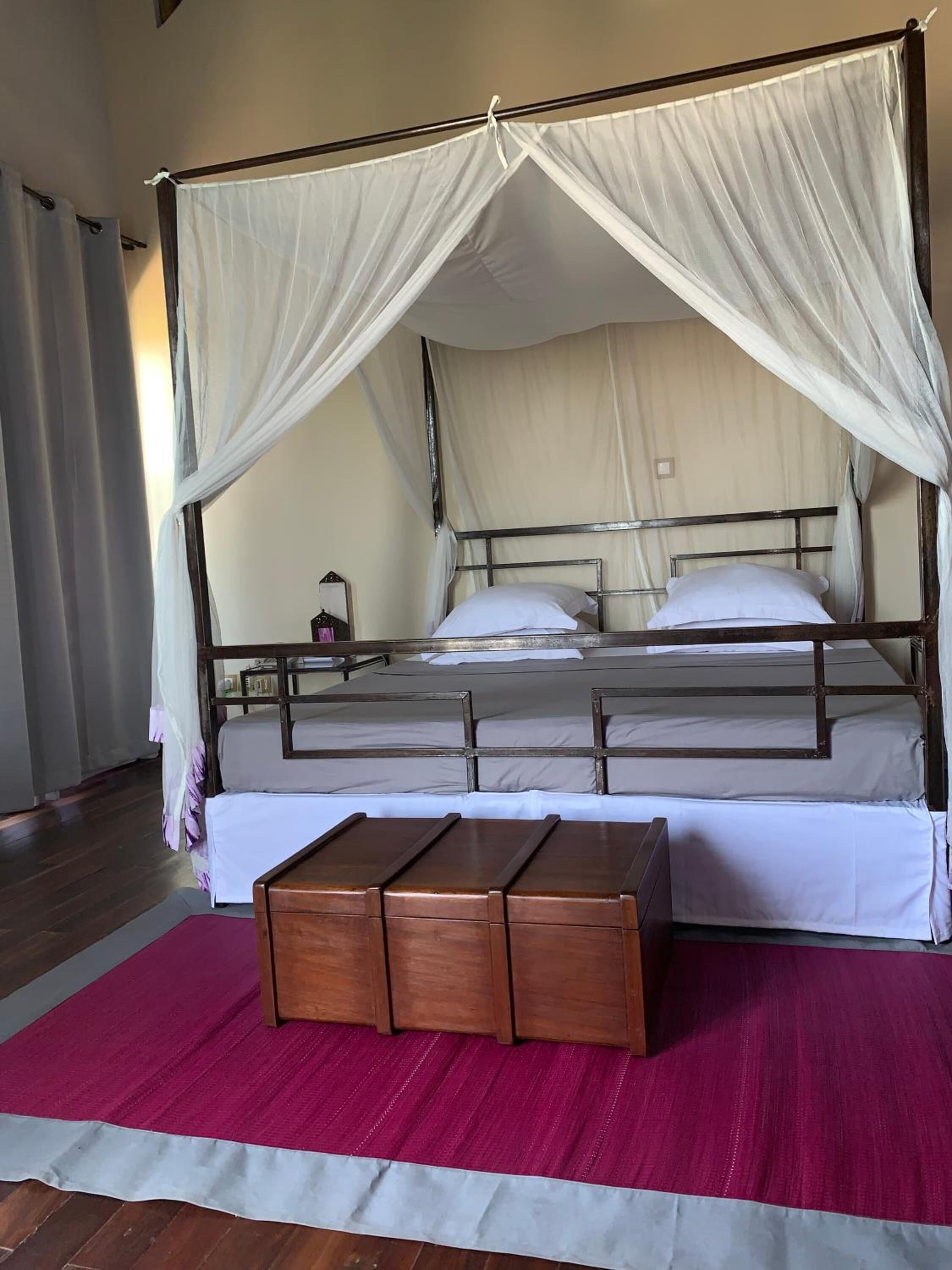 A bed with a canopy, a wooden bench, and a red rug.