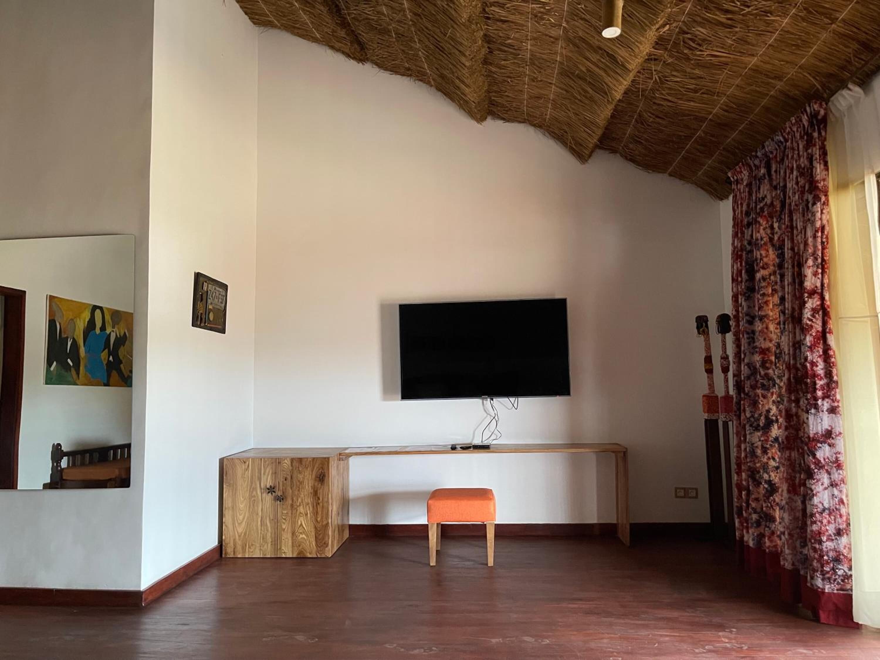 Una habitación con un escritorio de madera, un televisor fijado en la pared, un banco y un espejo en la pared izquierda.