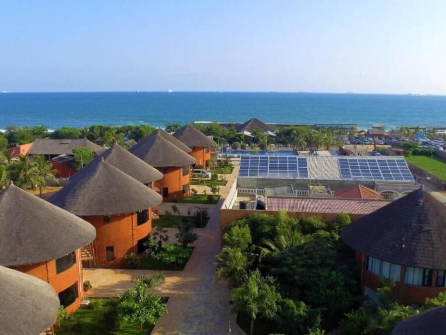 Un complexe hôtelier doté de bâtiments aux toits de chaume, d’une piscine équipée de panneaux solaires et offrant une vue sur l’océan.