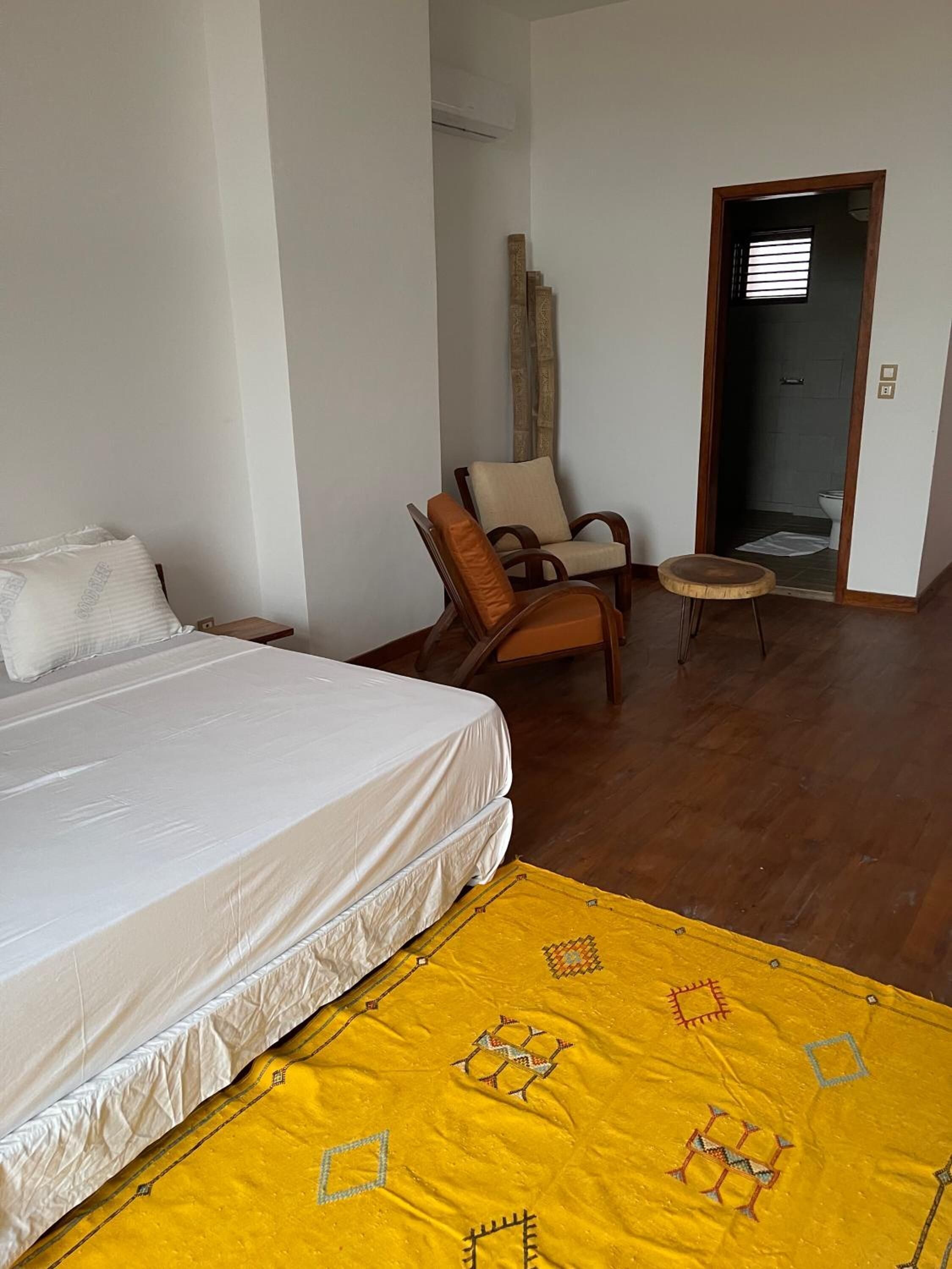 Een kamer met een bed, een stoel, een klein krukje en een deur naar een badkamer.