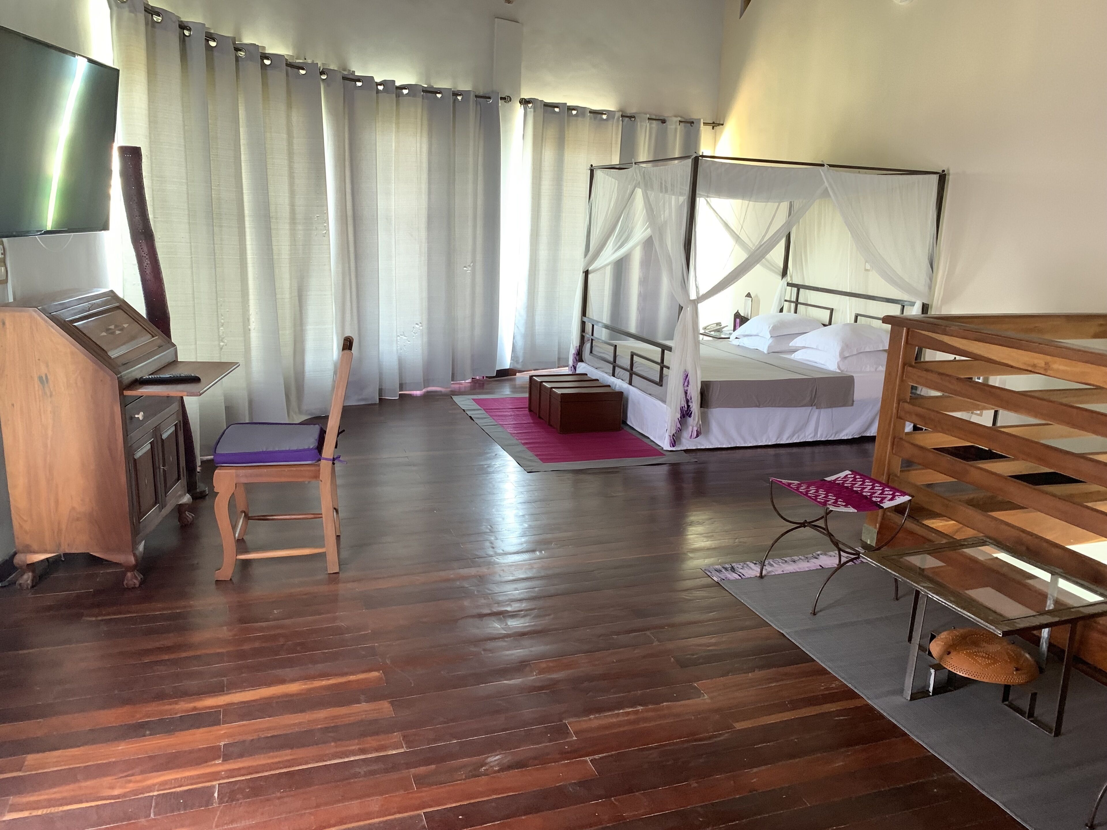 Ein Schlafzimmer mit einem hölzernen Bett, einem Nachttisch, einem Sessel, einem Schreibtisch mit Computer und einem Fernseher.