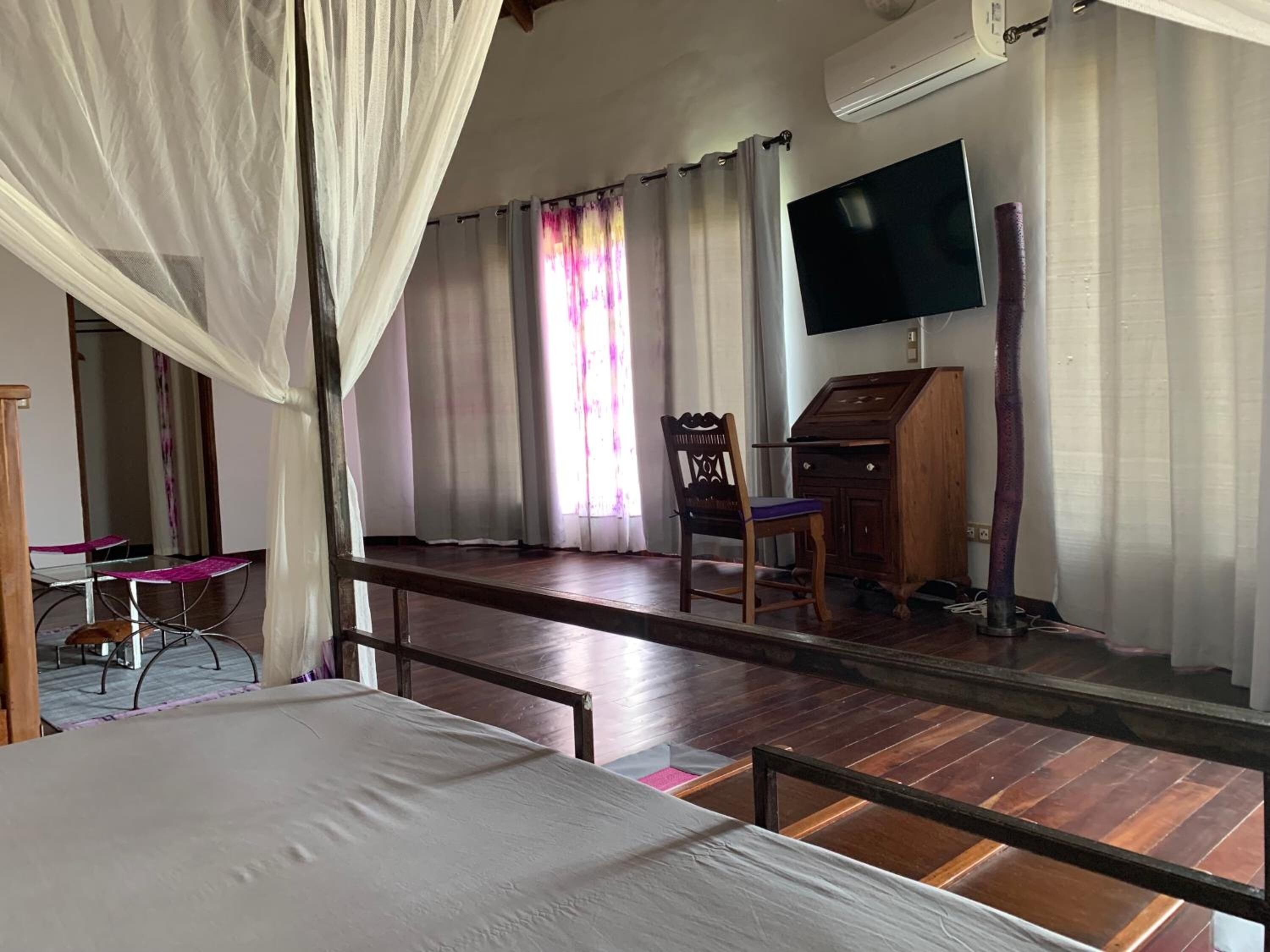 A hotel room with a bed, a desk, a chair, a TV, and a wooden cabinet.