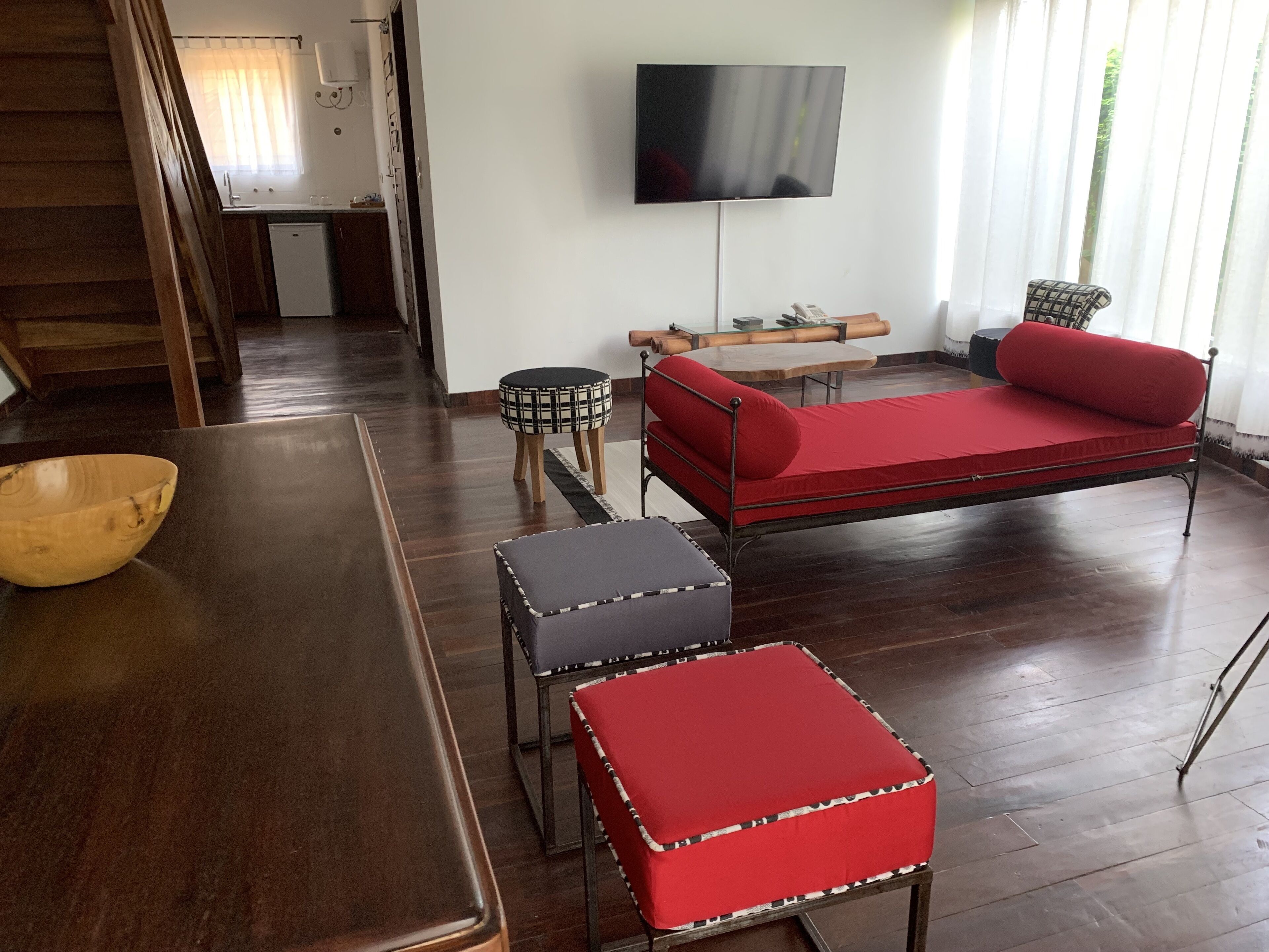 A modern living room with a sofa, ottomans, a wooden dining table, and a television mounted on the wall.
