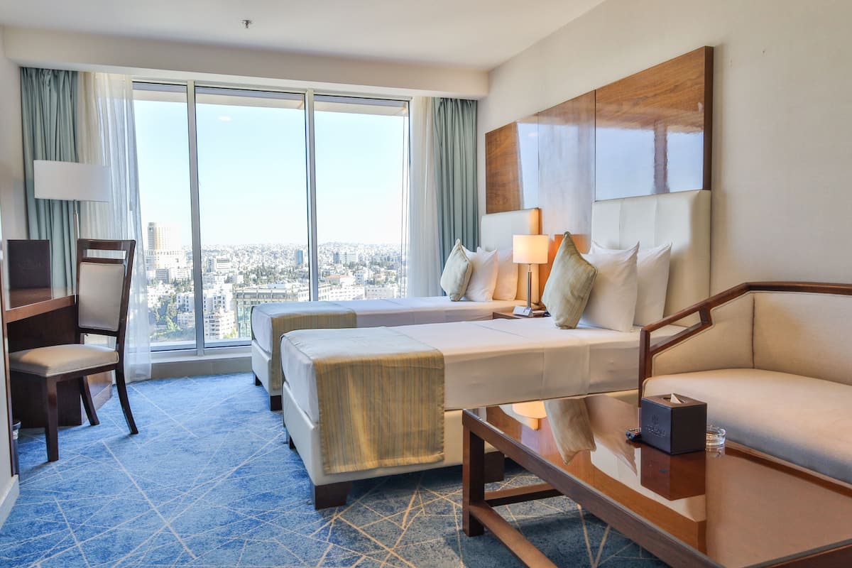 Une chambre d’hôtel avec une grande fenêtre, un lit, un canapé, un bureau et une chaise.