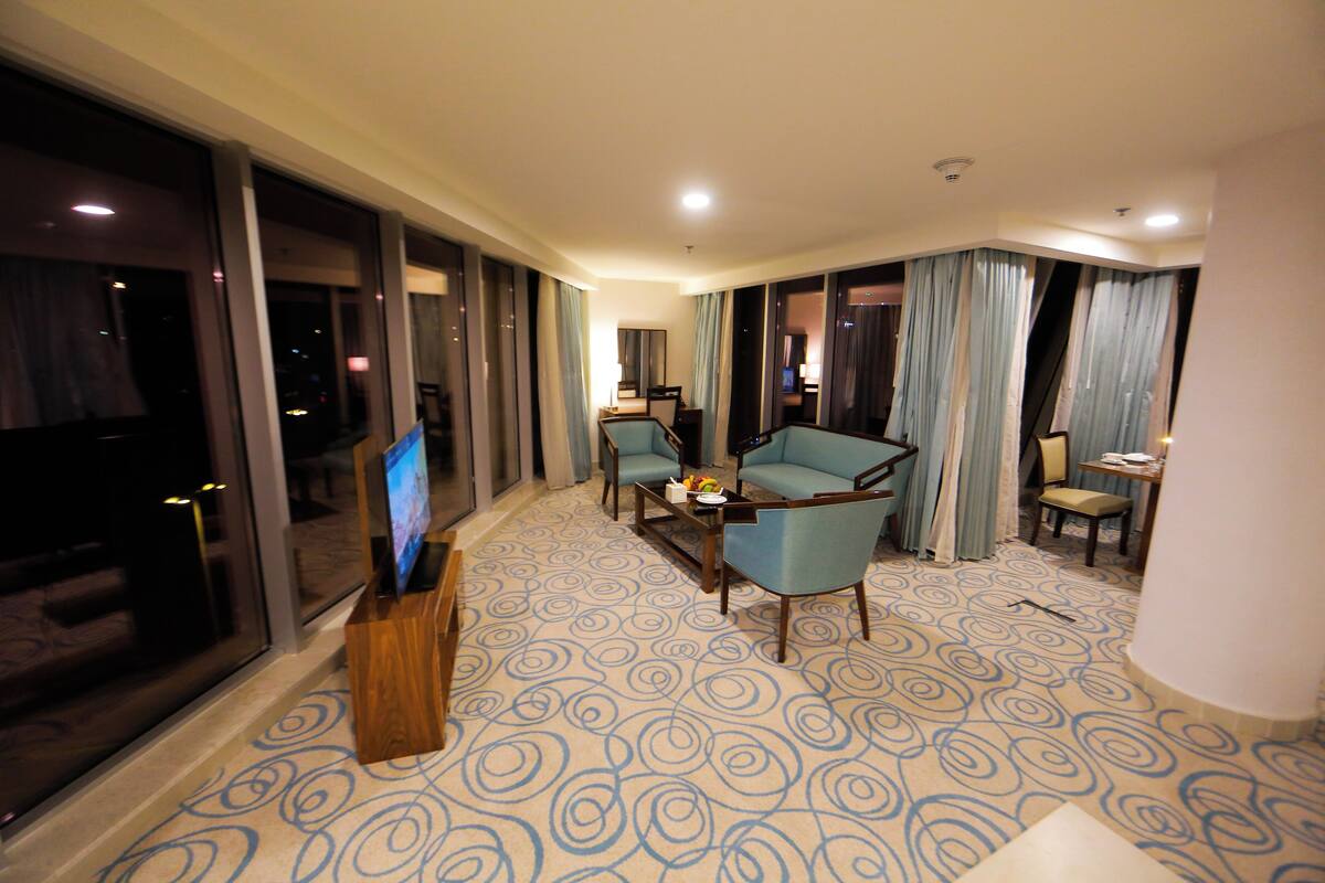 Une chambre d’hôtel avec une grande télévision, deux fauteuils, une petite table et un tapis à motifs.