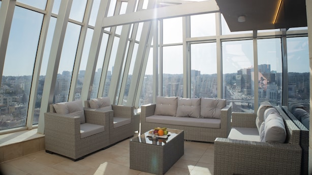Un intérieur moderne situé dans un immeuble de grande hauteur, avec vue sur la ville, des meubles en osier et une table basse en verre.