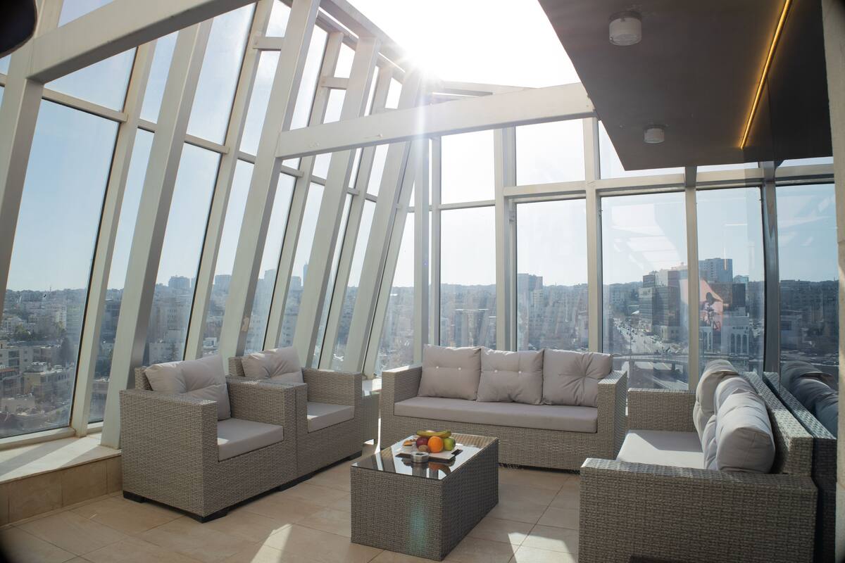 Un intérieur moderne situé dans un immeuble de grande hauteur, avec vue sur la ville, des meubles en osier et une table basse en verre.