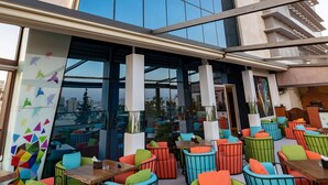 Un espace extérieur aménagé avec des chaises et des tables colorées, un bâtiment moderne doté de grandes fenêtres et une vue sur le paysage urbain.