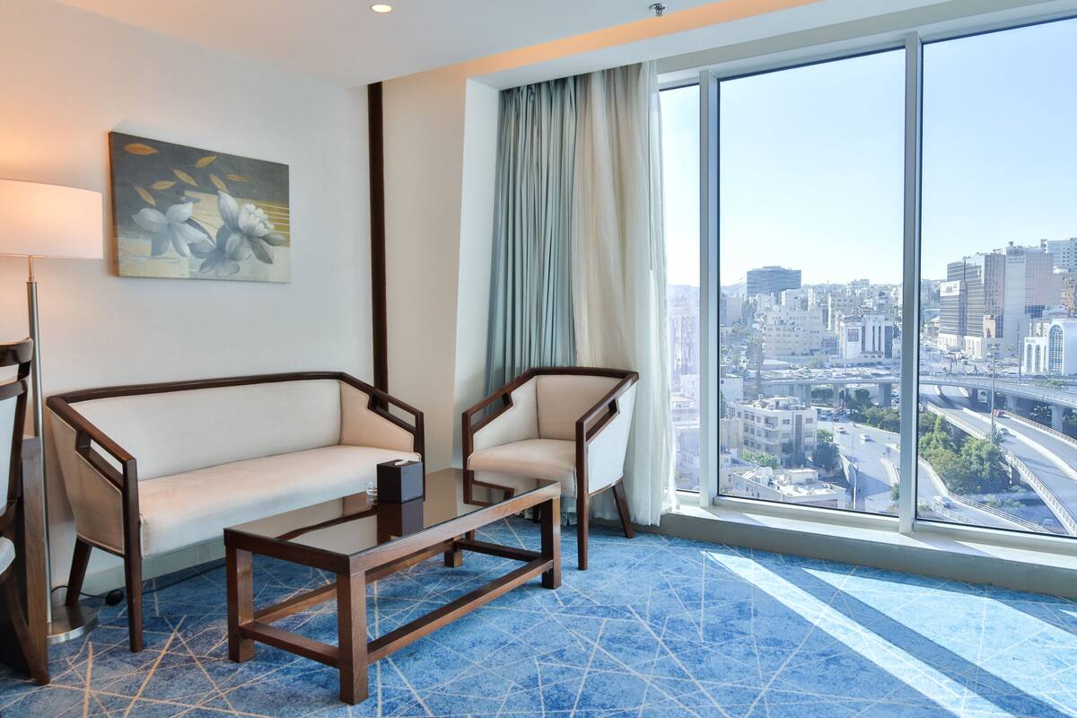 Une chambre d’hôtel moderne dotée d’une grande fenêtre donnant sur la ville, d’un canapé, d’une table basse et d’un tableau au mur.
