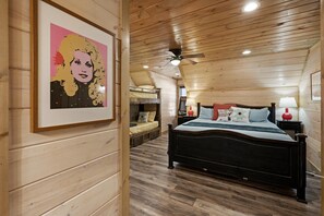 Ein Zimmer mit Holzwandverkleidung, einem Etagenbett, einem großen Bett mit Kissen und einem Deckenventilator.