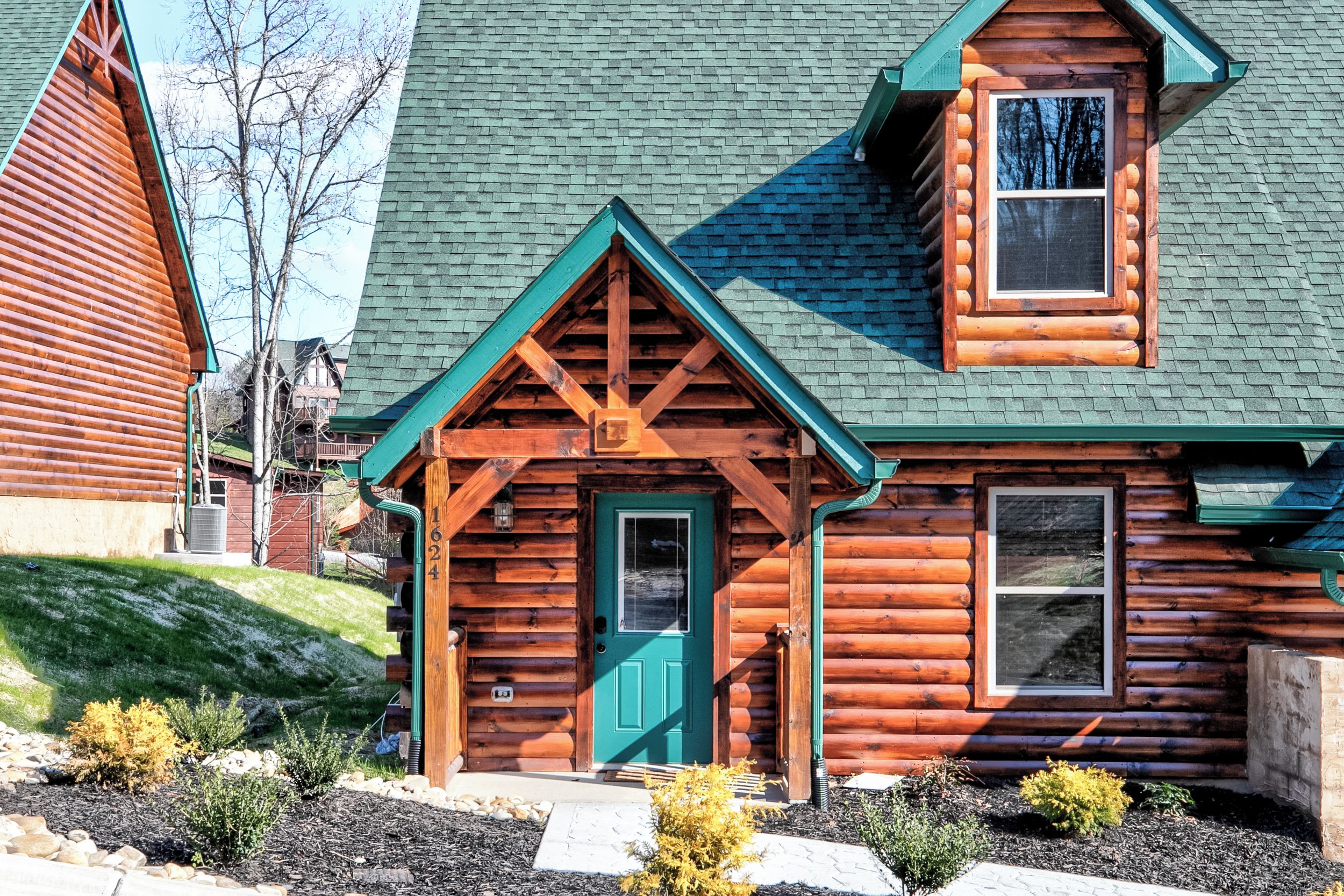 A log cabin with a green door, a small porch, and a chimney.