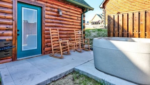 A log cabin with a turquoise door, a hot tub, and wooden rocking chairs outside.