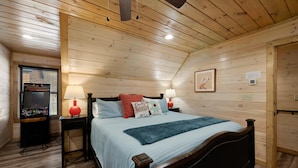 A wooden-paneled bedroom with a bed, two bedside tables, a lamp, a picture on the wall, and a window with blinds.