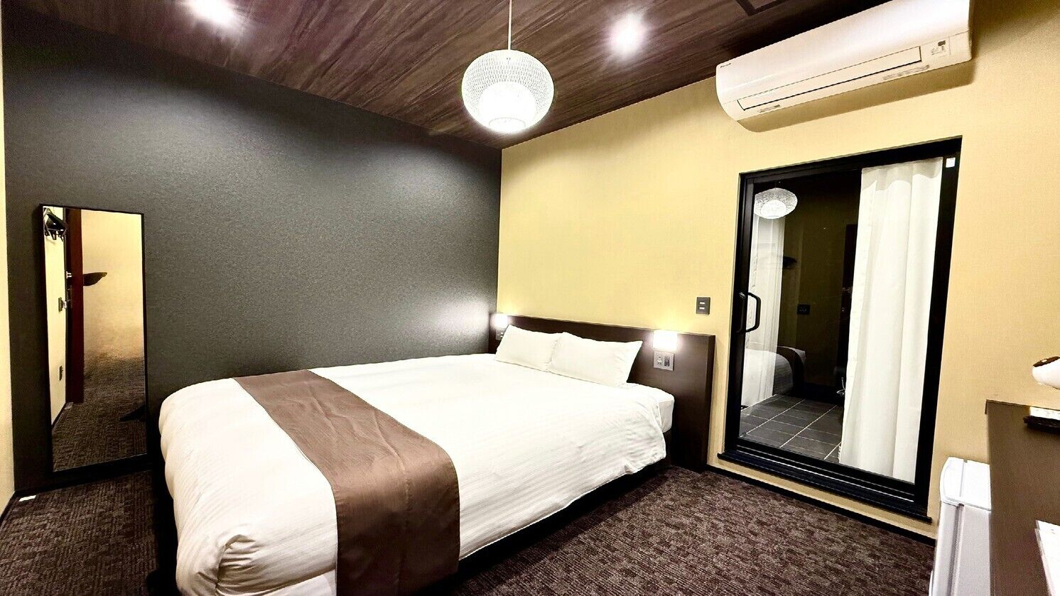 Quarto de hotel com cama, espelho, guarda-roupa e ar condicionado.