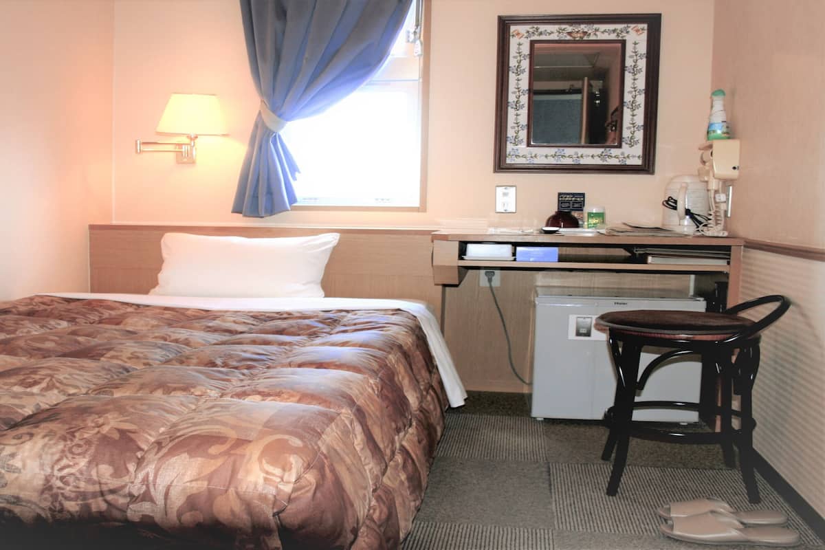 Une chambre d’hôtel équipée d’un lit, d’un bureau, d’une chaise, d’un petit réfrigérateur et d’un miroir au mur.