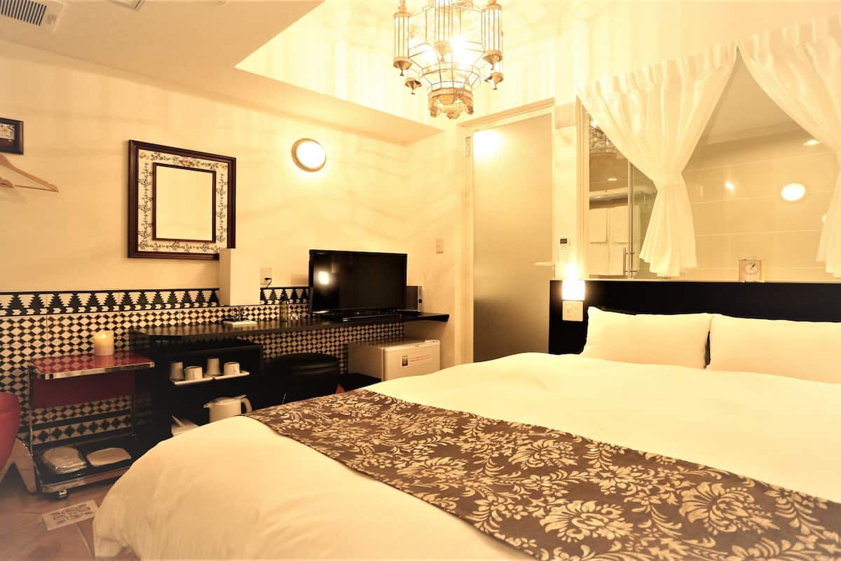 Une chambre d’hôtel équipée d’un lit, d’une télévision, d’un minibar, d’un miroir et d’un lustre.