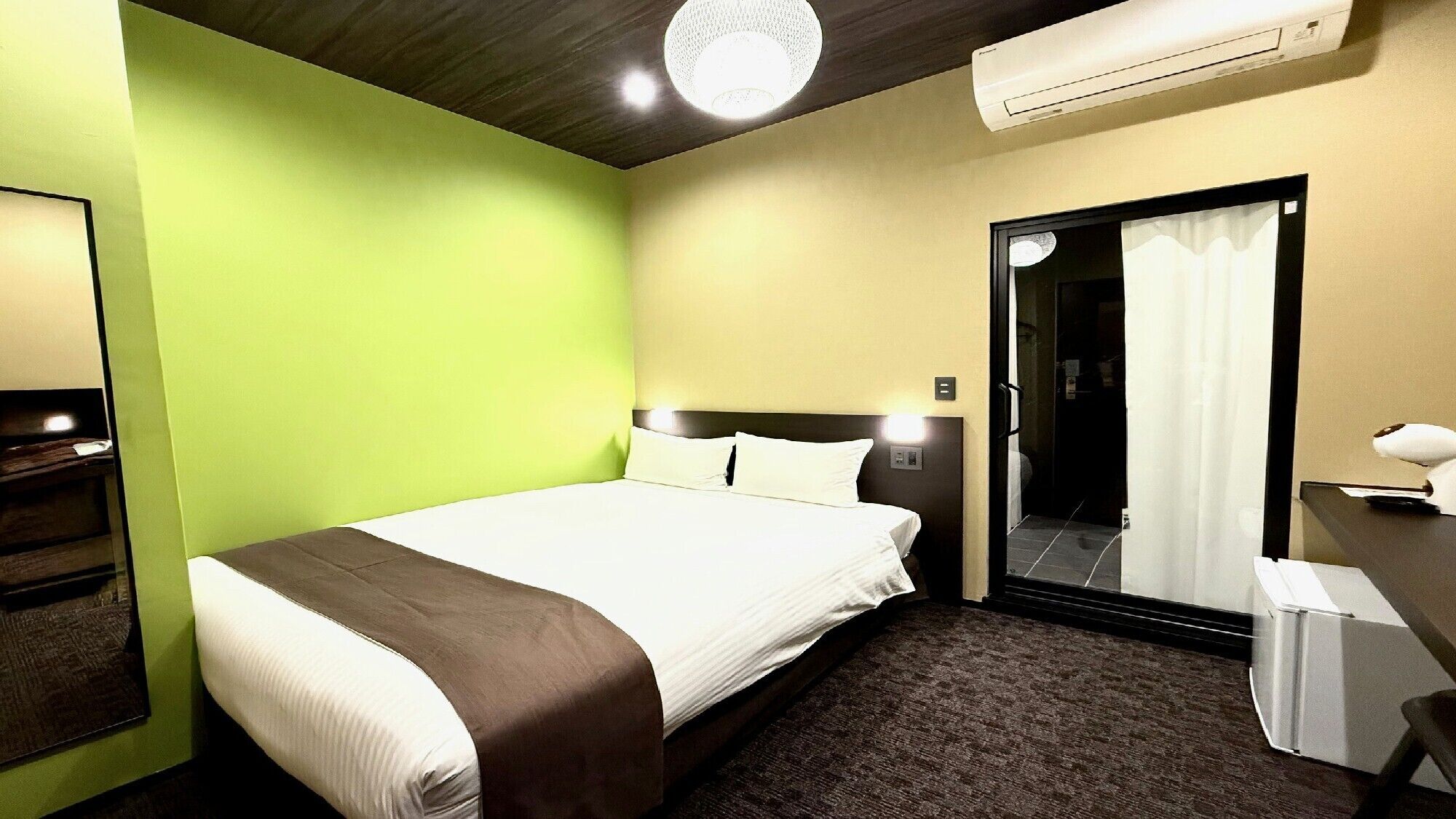 Quarto de hotel com cama, espelho, ar-condicionado e porta para um banheiro.