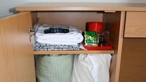 Ein Hotelzimmer mit einem Holzkästen, der ein gefaltetes Handtuch, Pantoffeln, eine grüne Flasche und eine rote Tasse enthält.