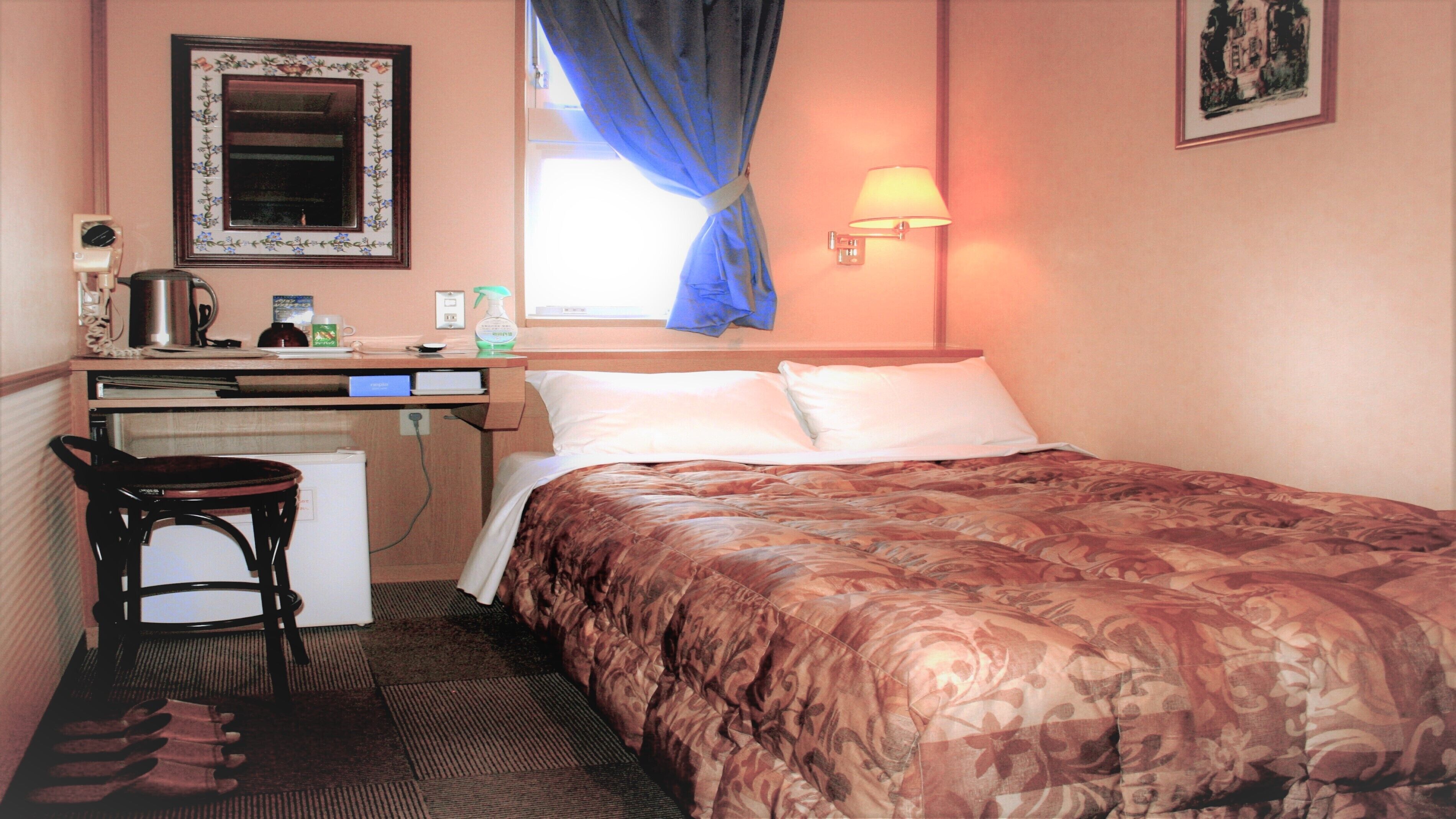 Quarto de hotel com cama, escrivaninha, cadeira e janela com cortinas.